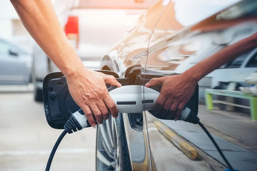 A hand plugging an EV charger into a car.