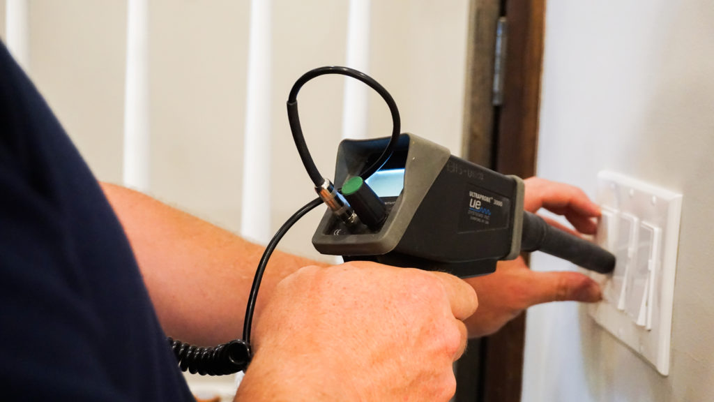 An electrical inspector using an assessment tool on light switches.