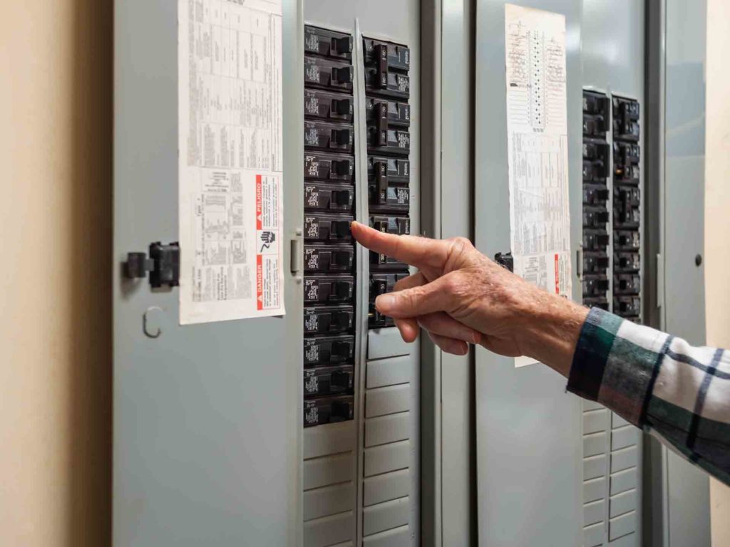 An electrician shutting off power at a circuit breaker box.